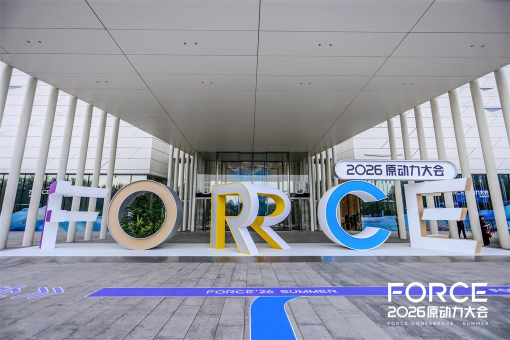 图片展示了2026火山引擎FORCE原动力大会的会场入口。入口处有大型彩色字母装饰,以白色、黄色、蓝色为主,拼出“FORCE”字样。上方悬挂着“2026原动力大会”的标识牌。地面铺有蓝色和白色图案的地毯,入口两侧设有柱子。该图片与上下文紧密相关,直观呈现了大会现场的场景,体现了大会的规模和氛围。
