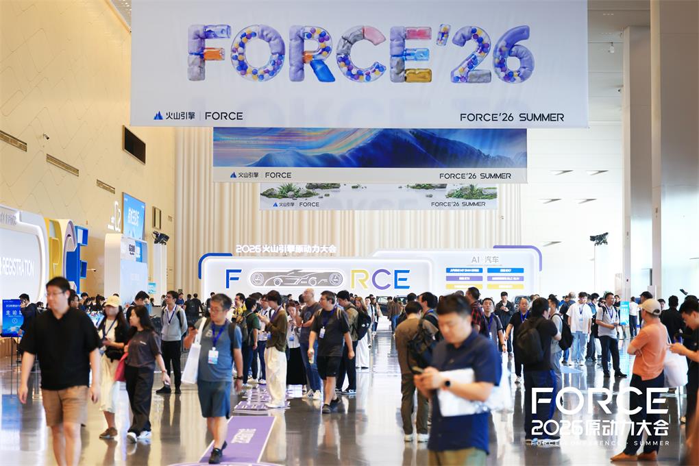 这张图片展示的是2026火山引擎FORCE原动力大会的现场场景。画面中有大量参会人员在宽敞的会议场馆内活动走动,场馆上方悬挂着醒目的“FORCE’26”标识,还设置了印有“FORCE 26 SUMMER”等字样的展示区域,场馆内的布置贴合大会主题,整体氛围热闹,体现出这场产业大会的规模与热度,与文档中大会集中发布AI相关技术成果的内容相呼应,直观呈现了大会现场的互动感与行业交流的氛围。