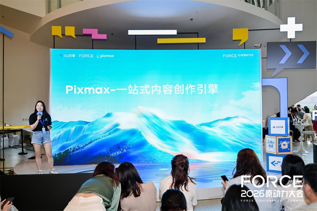 这张图片是Pixmax受邀参加2026火山引擎FORCE原动力大会的现场照片,画面左侧有一位手持麦克风的女士站在舞台上,舞台背景的大屏展示着“Pixmax-一站式内容创作引擎”的字样,大屏上还呈现蓝色山水风格的图案,大屏顶部可见“火山引擎 FORCE pixmax”的标识,画面右下角标注有“FORCE 2026原动力大会”的字样,舞台下方有不少参会人员,有的在看向舞台,有的在使用手机,整体呈现出会议分享的场景。
